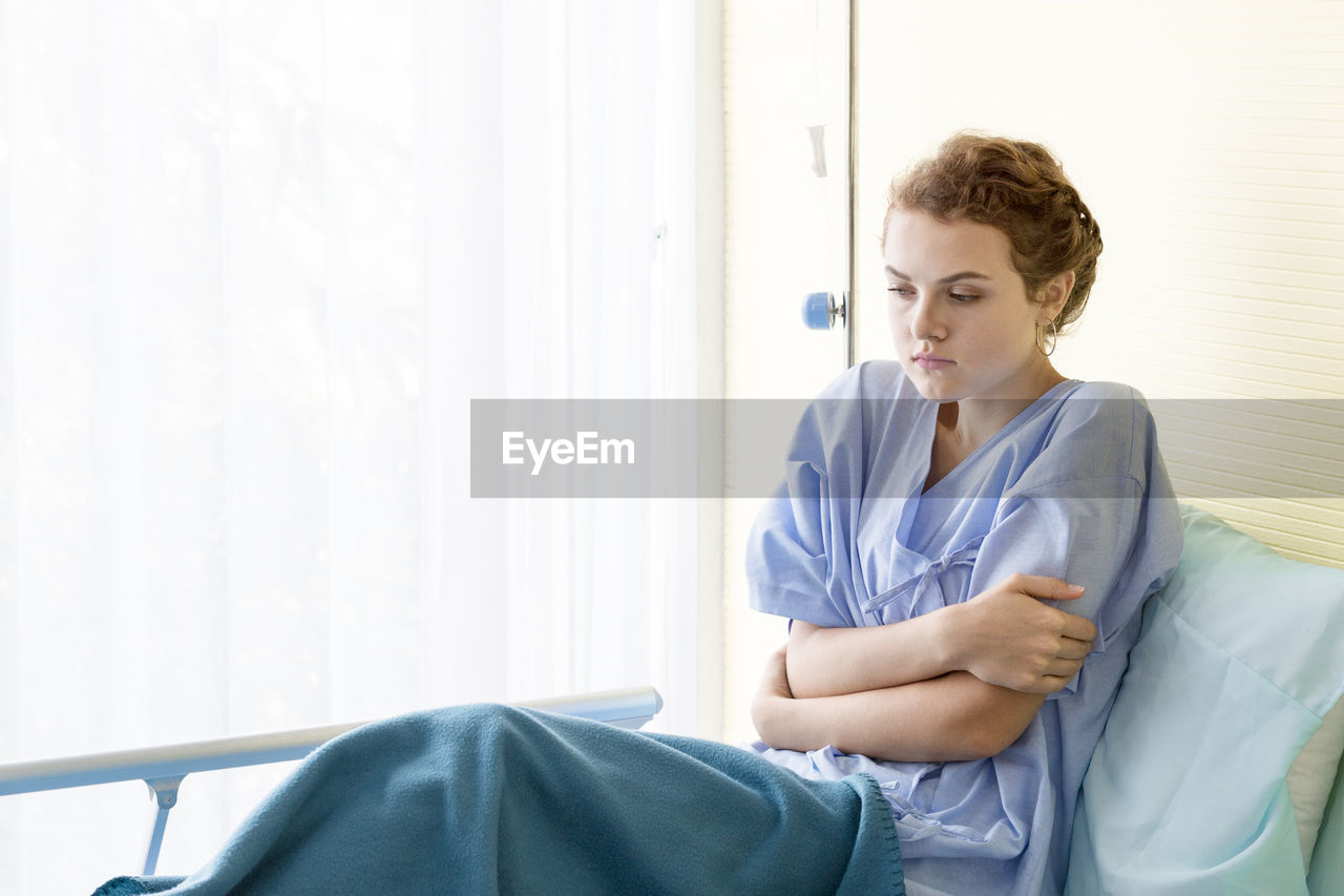 Young patient sitting on bed at hospital ward