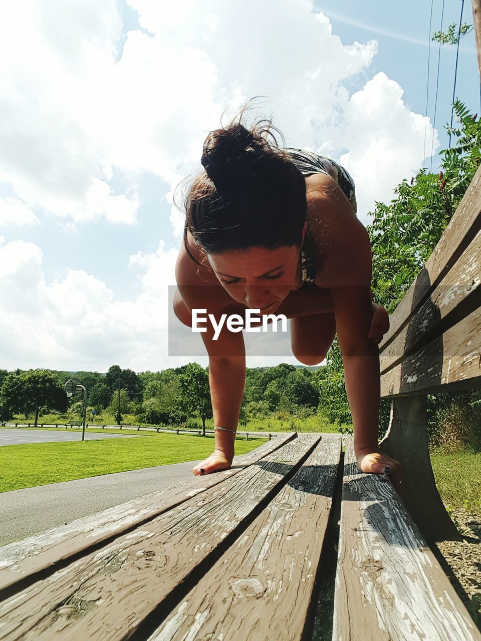 Full length of woman performing yoga on wooden bench against sky