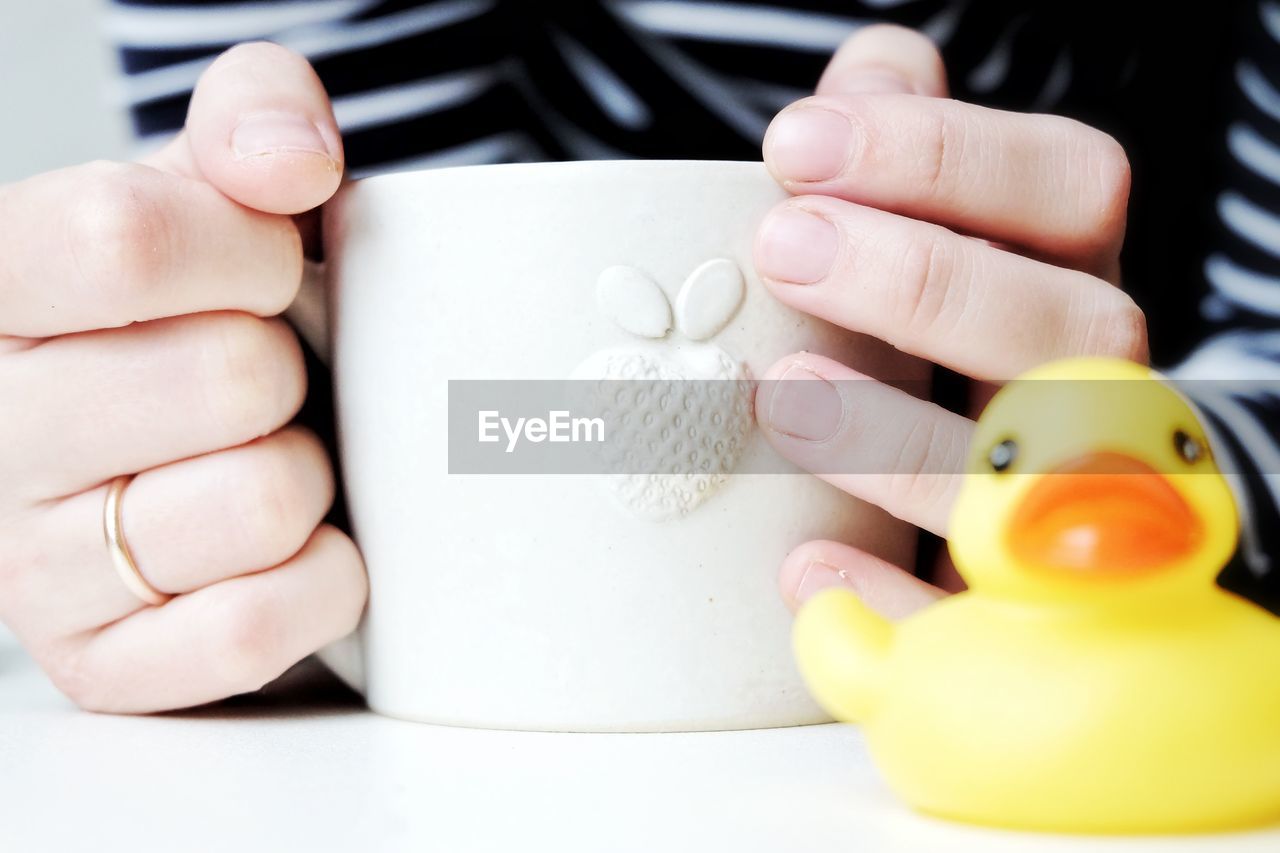 Close-up of hand holding coffee cup with toy animal in foreground