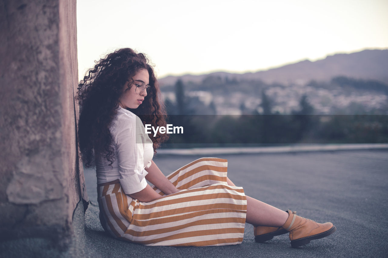 Young woman with curly hair looking away while sitting outdoors 