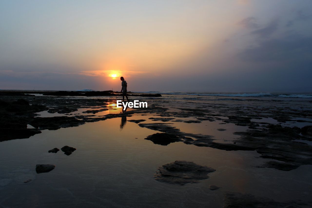 SILHOUETTE MAN STANDING ON BEACH DURING SUNSET