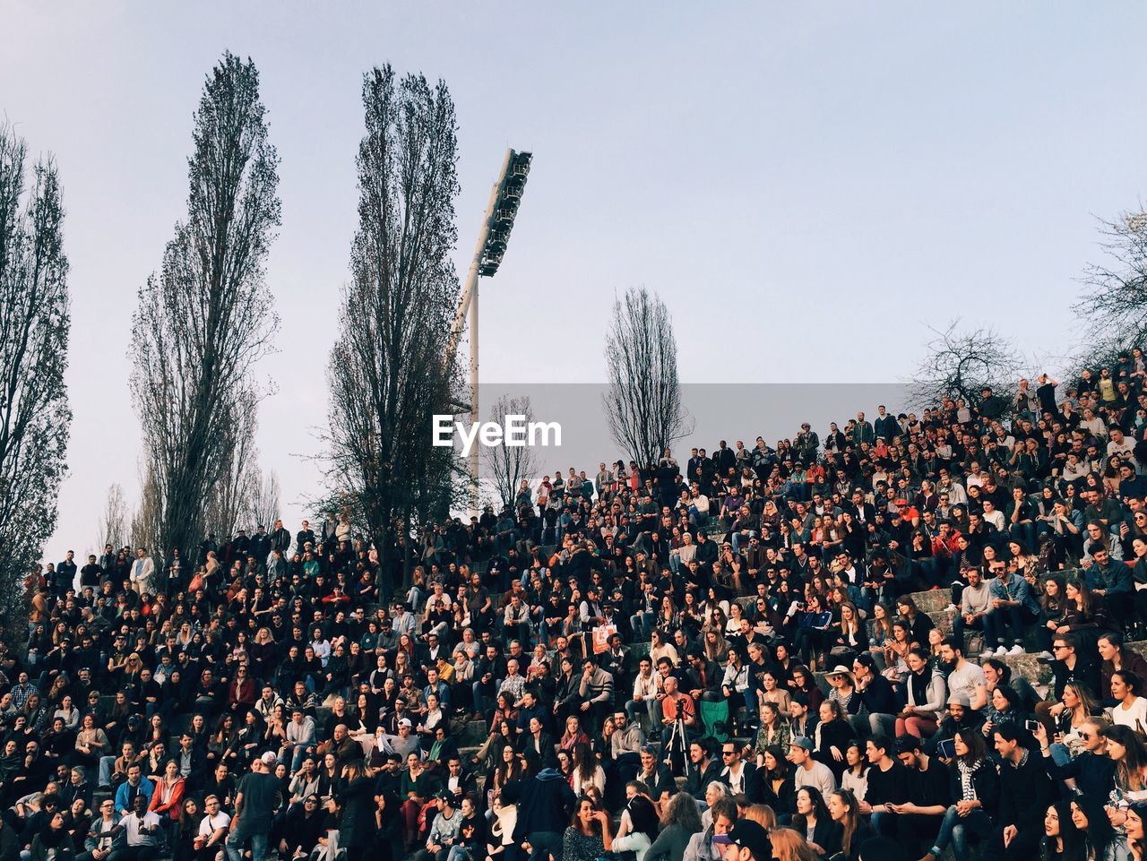 Crowd on grassy field against sky at mauerpark