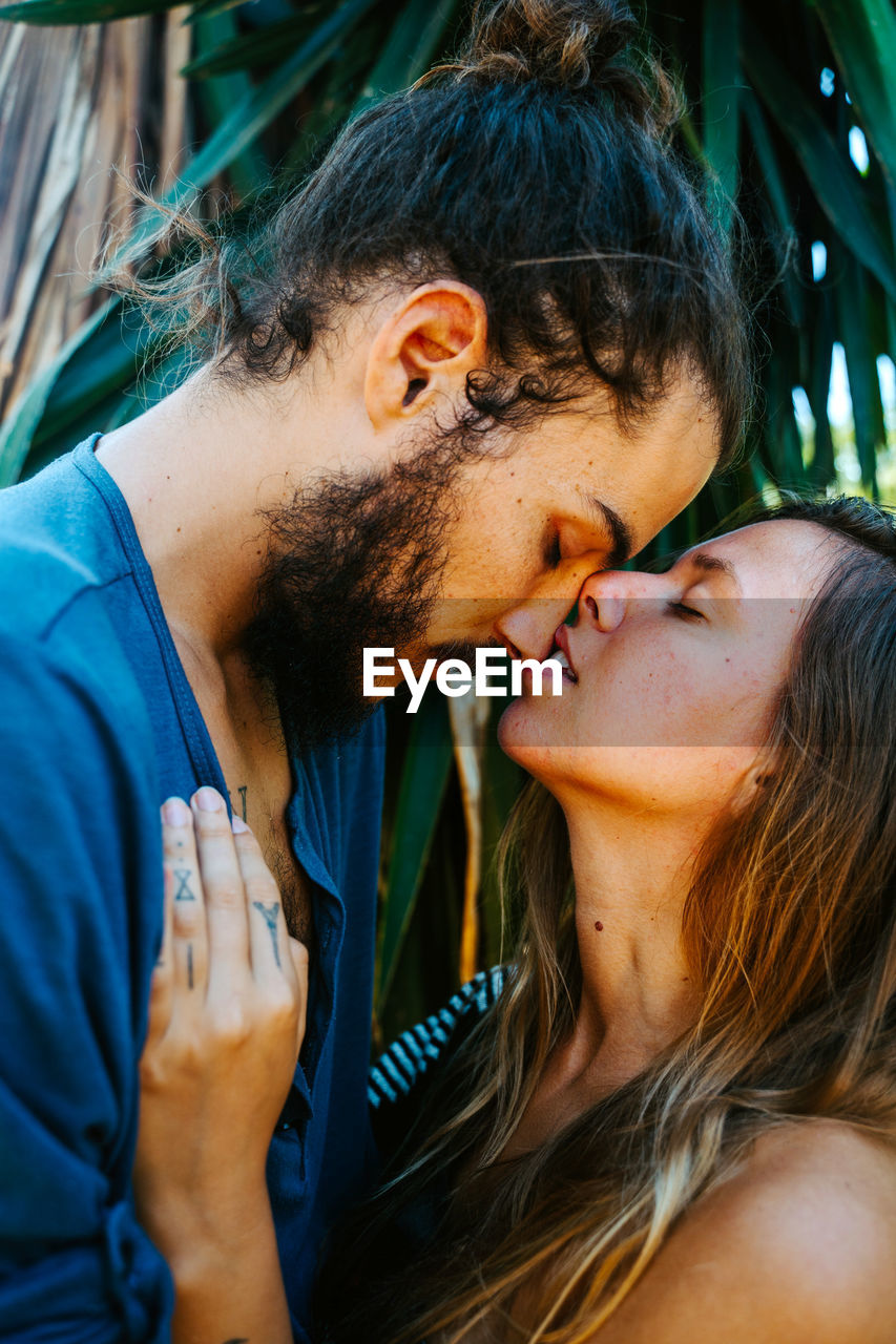 Side view of gentle multiethnic couple standing face to face with closed eyes and enjoying romantic moments in tropical park