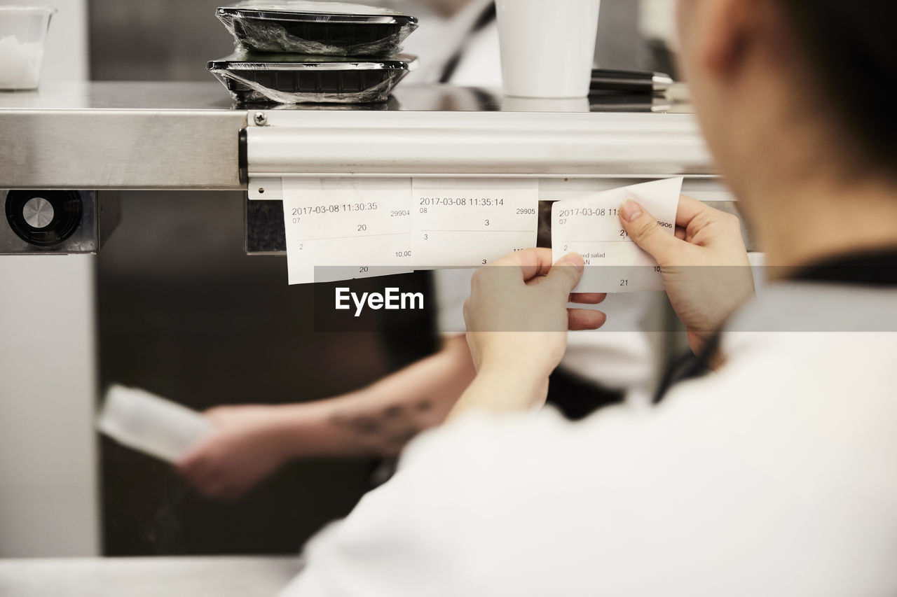 Cropped image of female chef reading order tickets in commercial kitchen