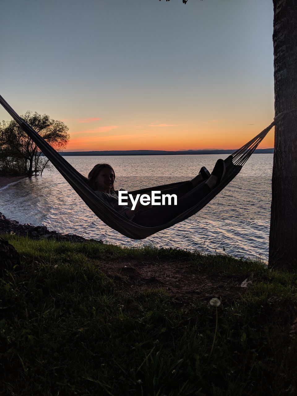 Girl relaxing in hammock against sea and sky during sunset