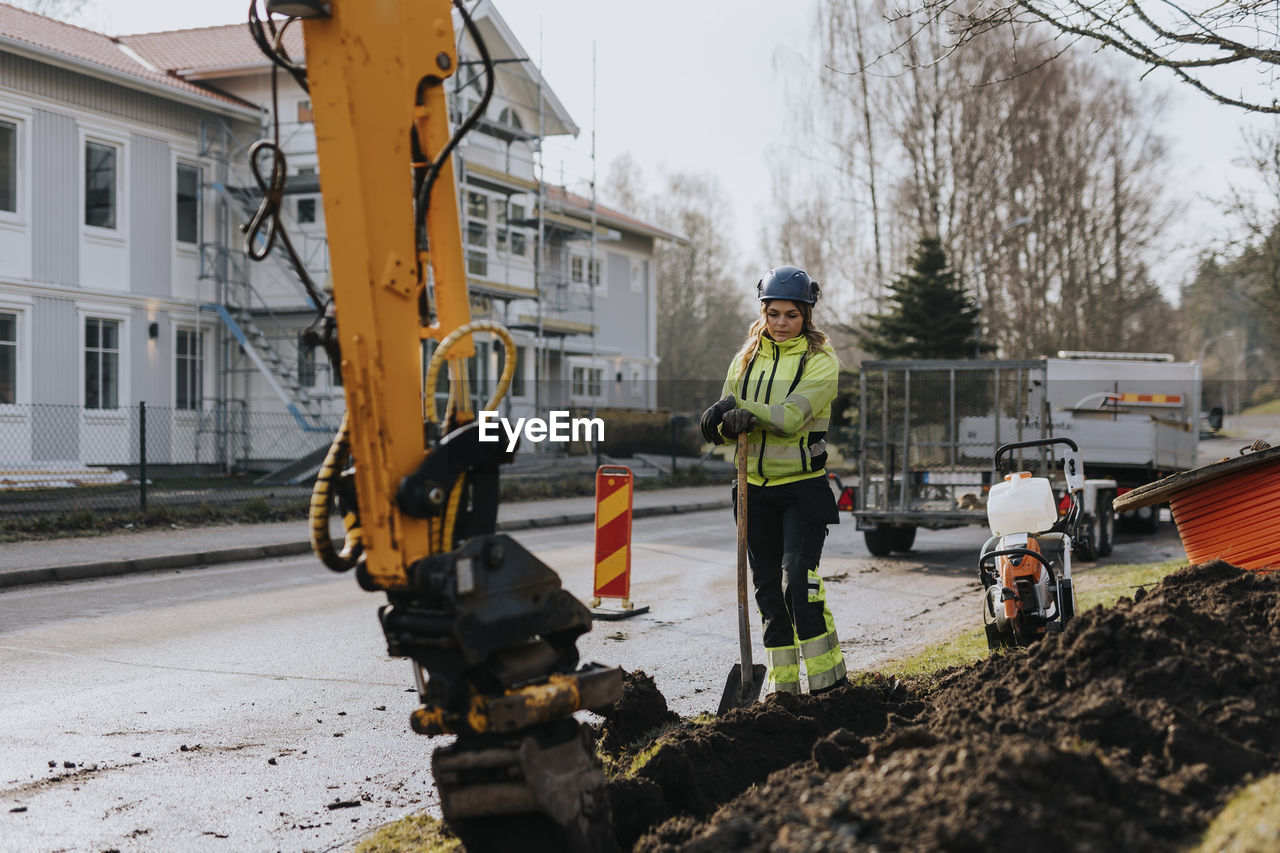 Female road worker and excavator at digging site