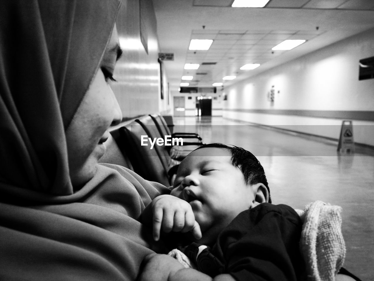 Side view of woman with baby girl sitting on bench in hospital