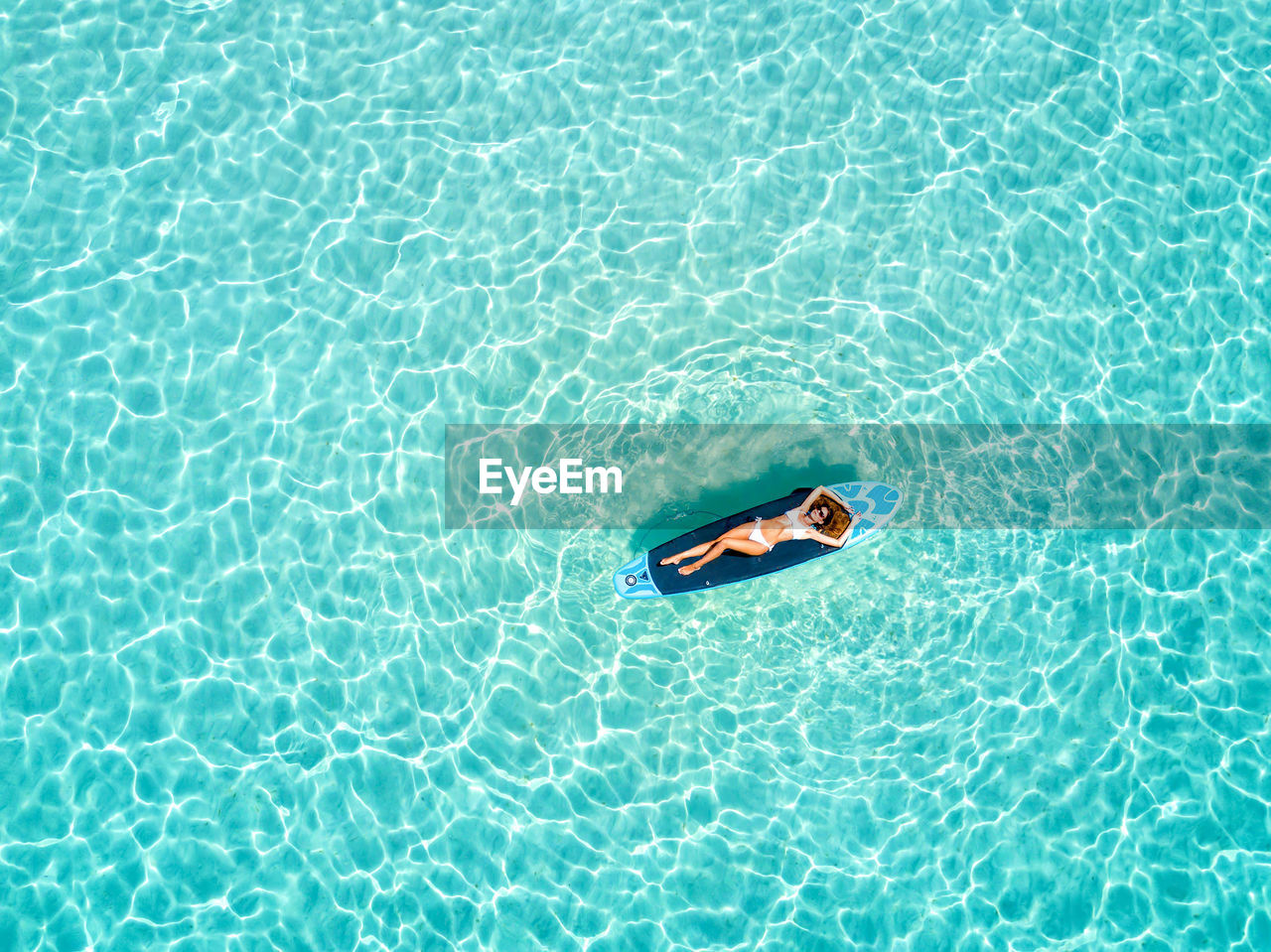 High angle view of woman floating on surfboard over sea