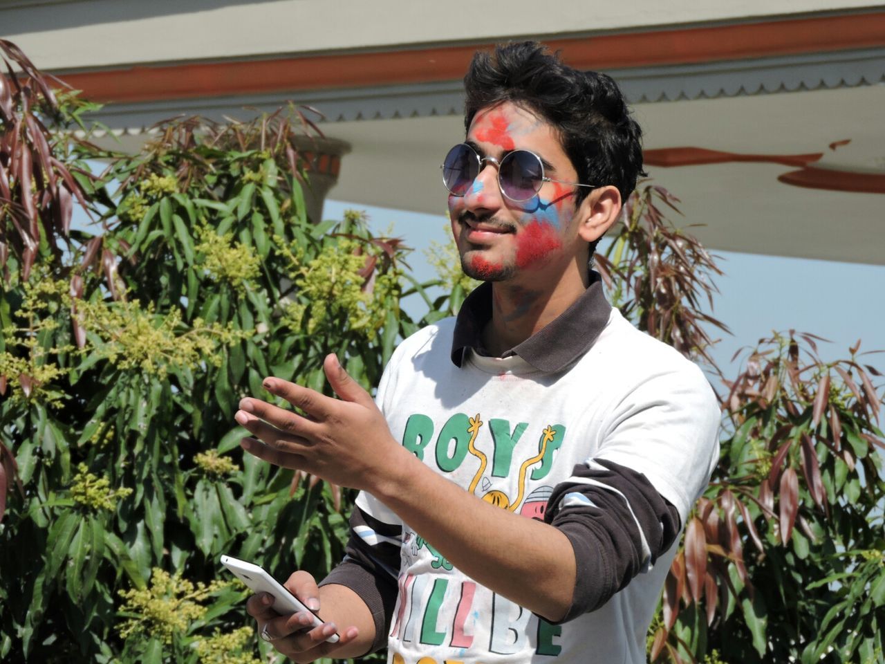 Young man with powder paint on face holding mobile phone while gesturing