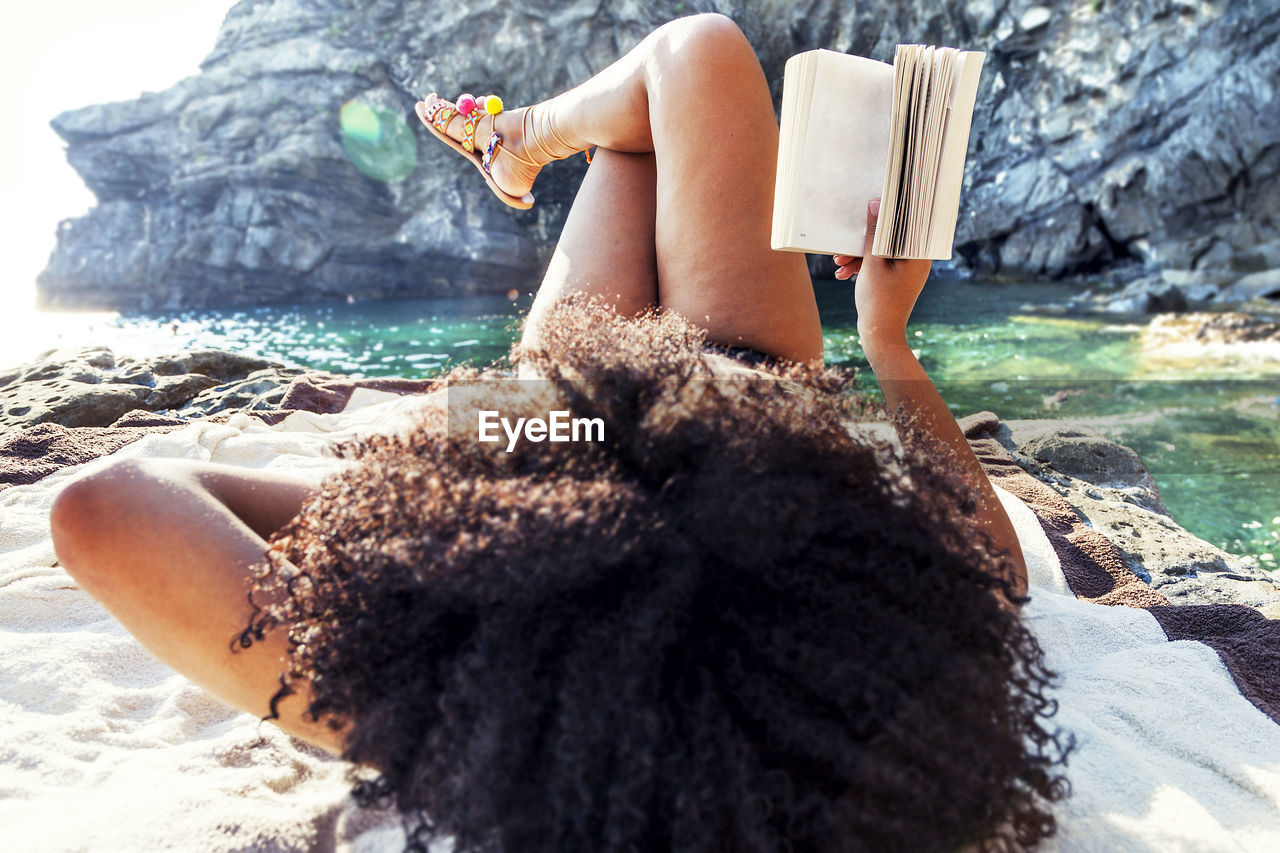 Woman reading book while lying at beach