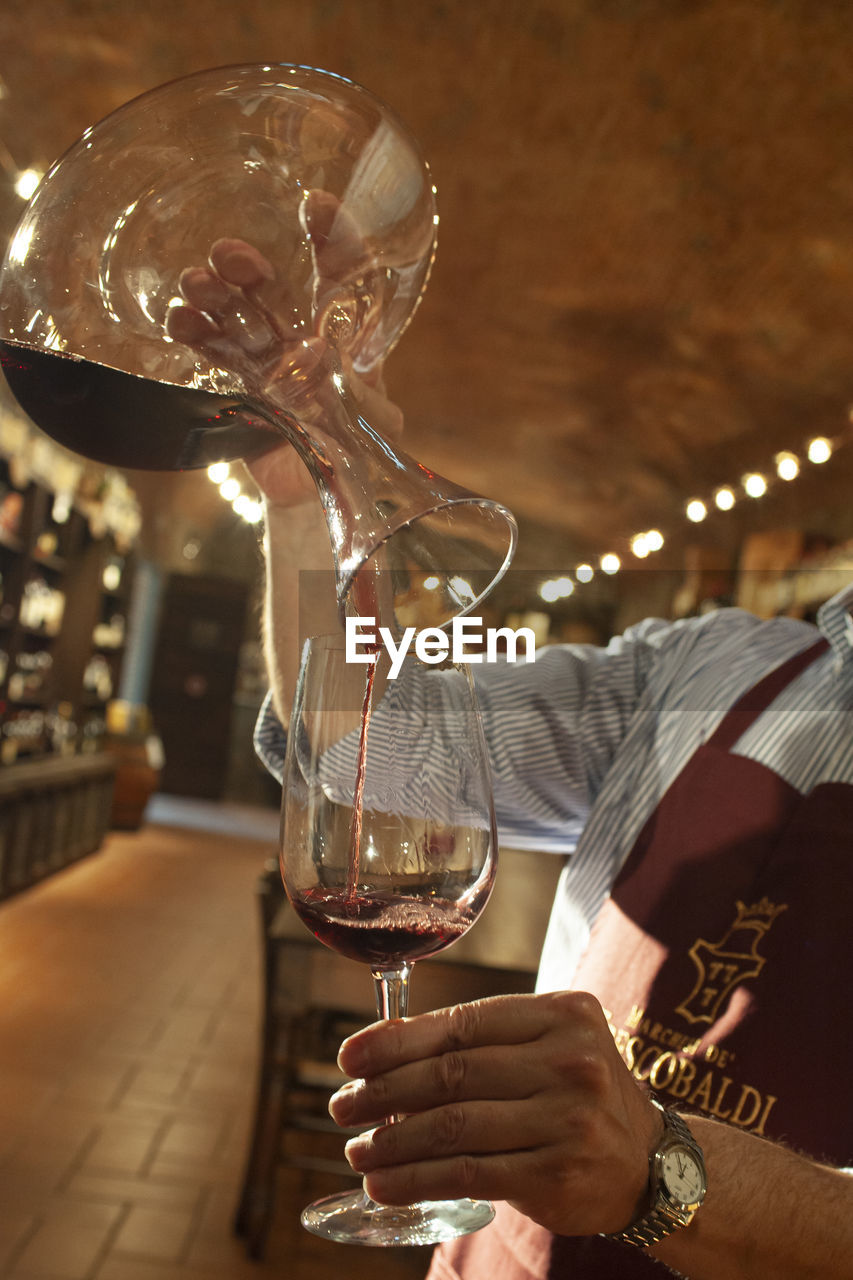 MIDSECTION OF MAN HOLDING GLASS OF ILLUMINATED WINE