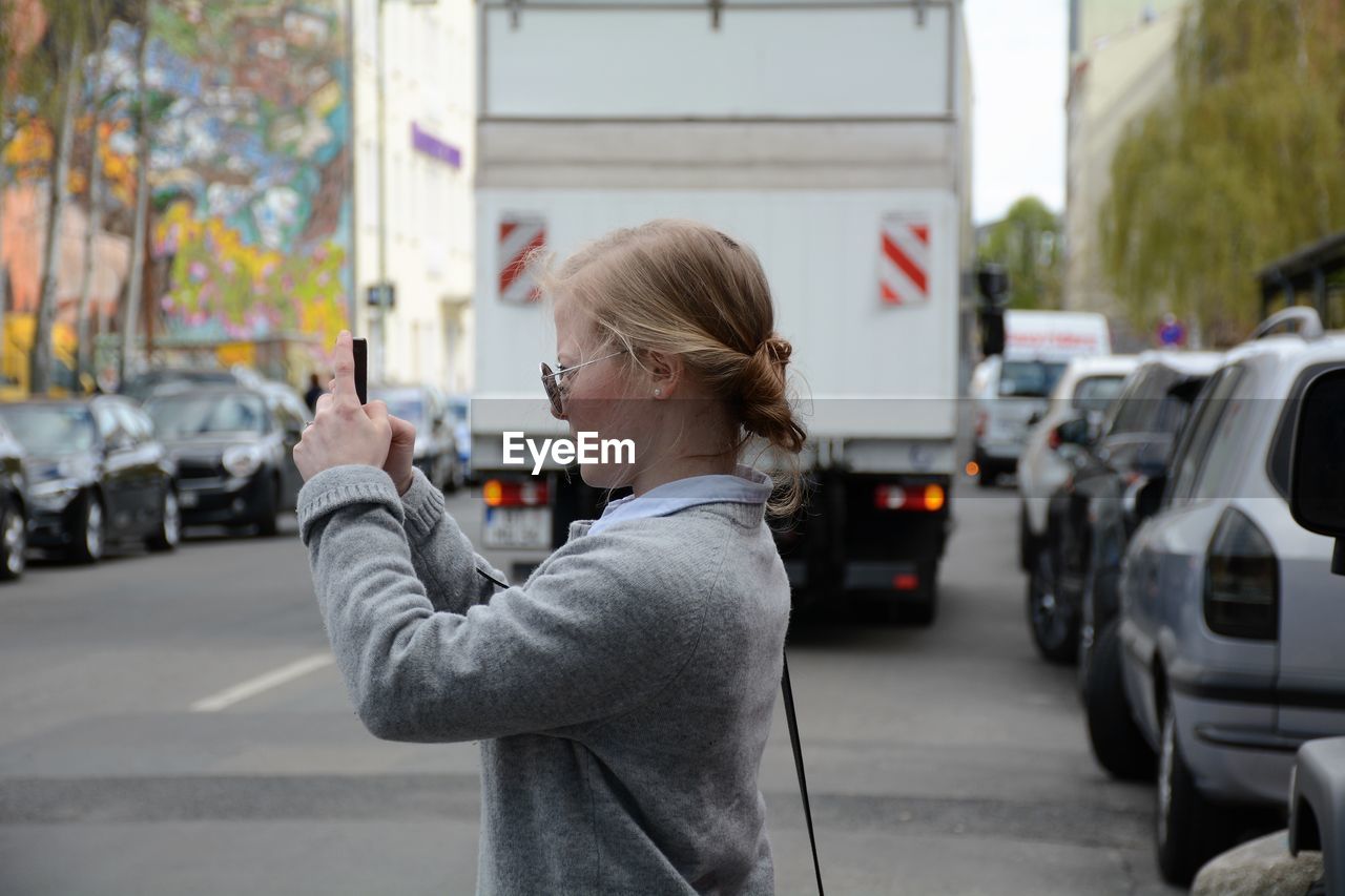 Side view of woman photographing on city street