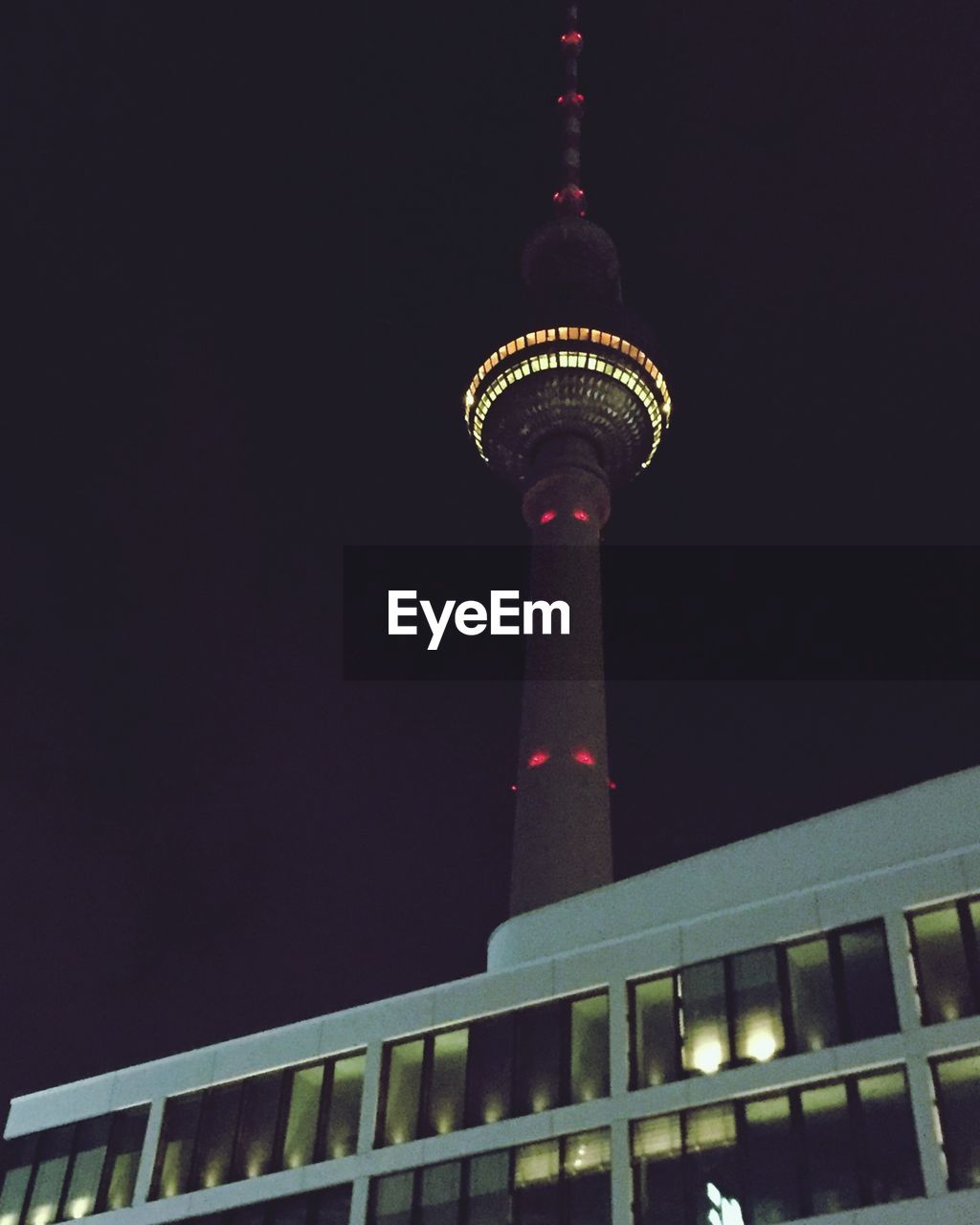 LOW ANGLE VIEW OF ILLUMINATED TOWER AGAINST SKY AT DUSK