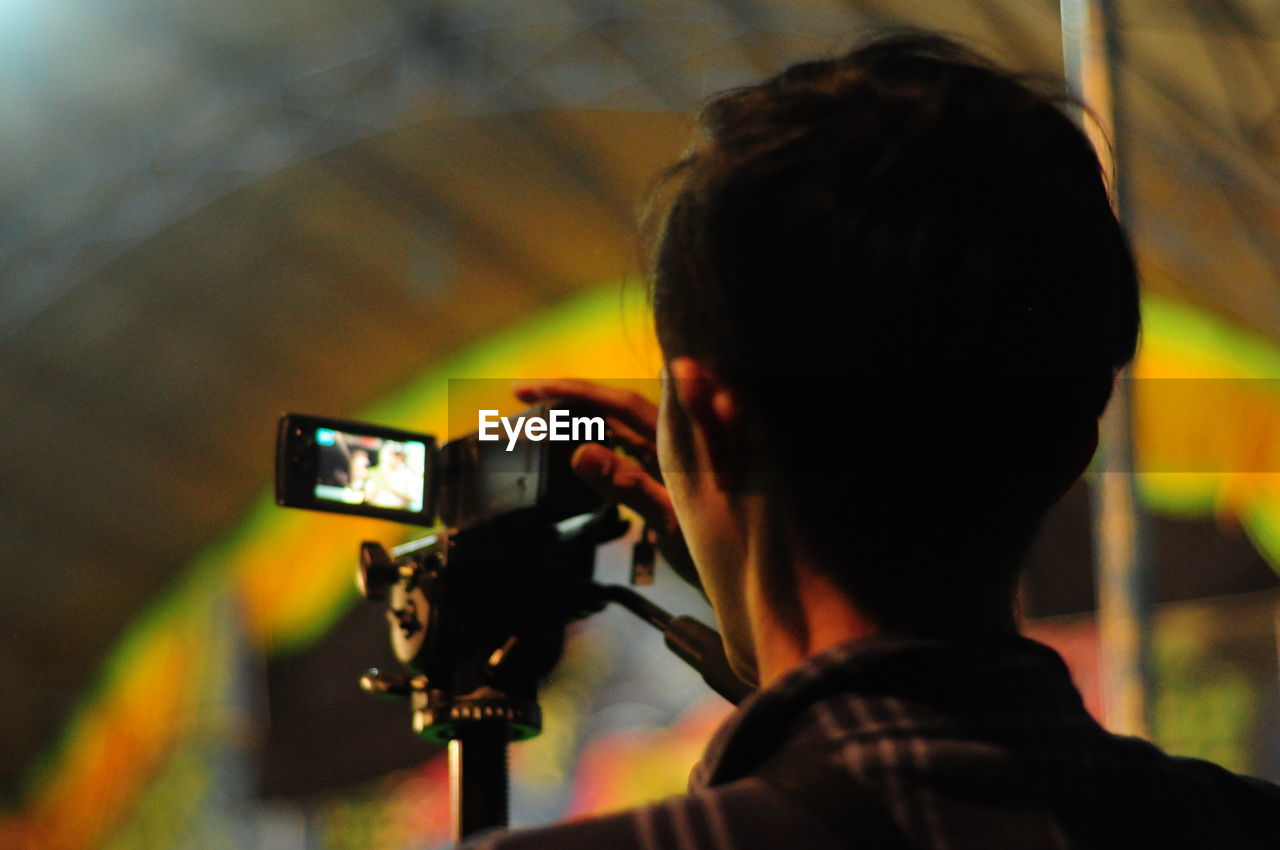 REAR VIEW OF MAN PHOTOGRAPHING CAMERA