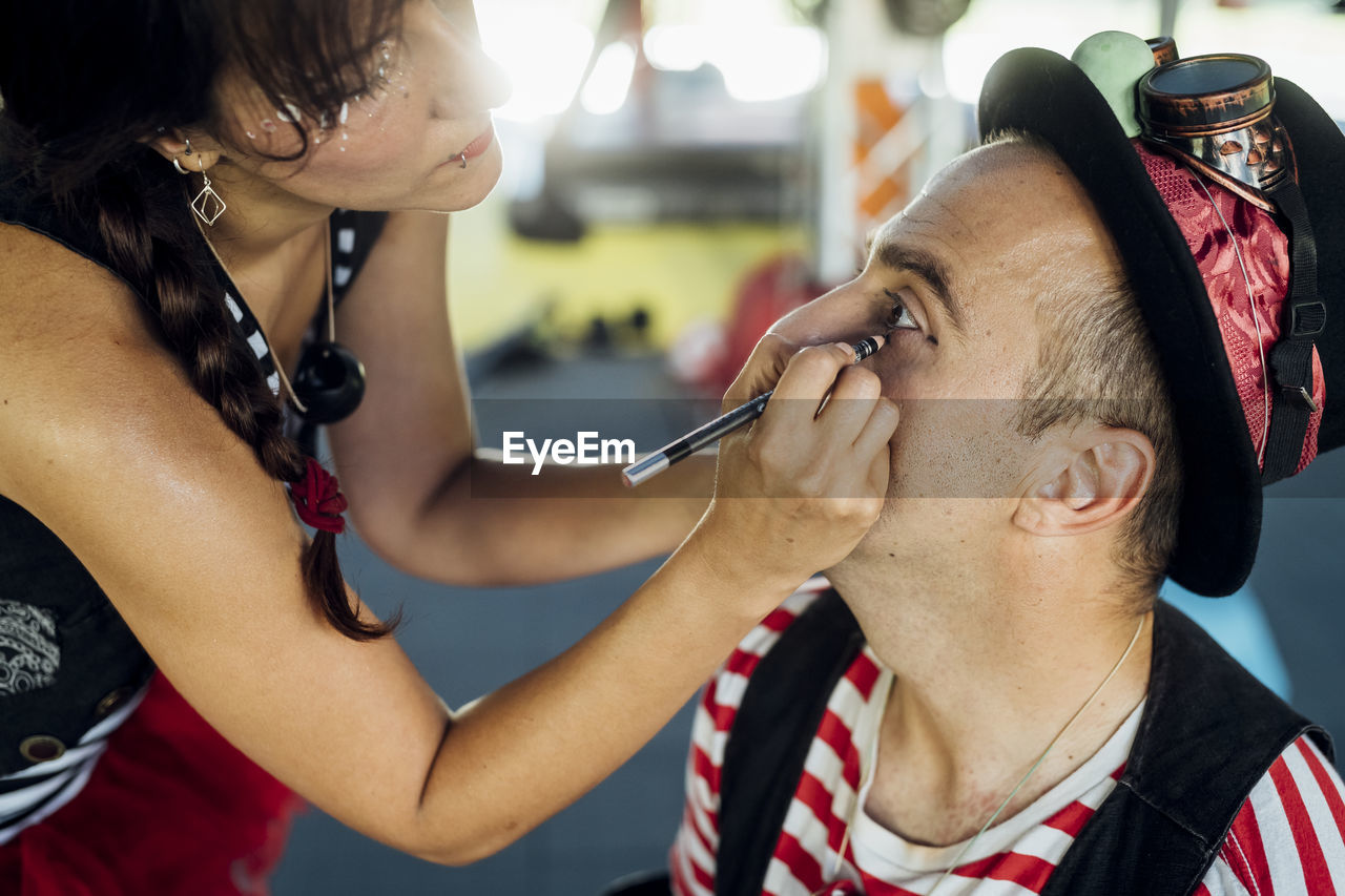 Female make-up artist applying eyeliner to male artist at backstage