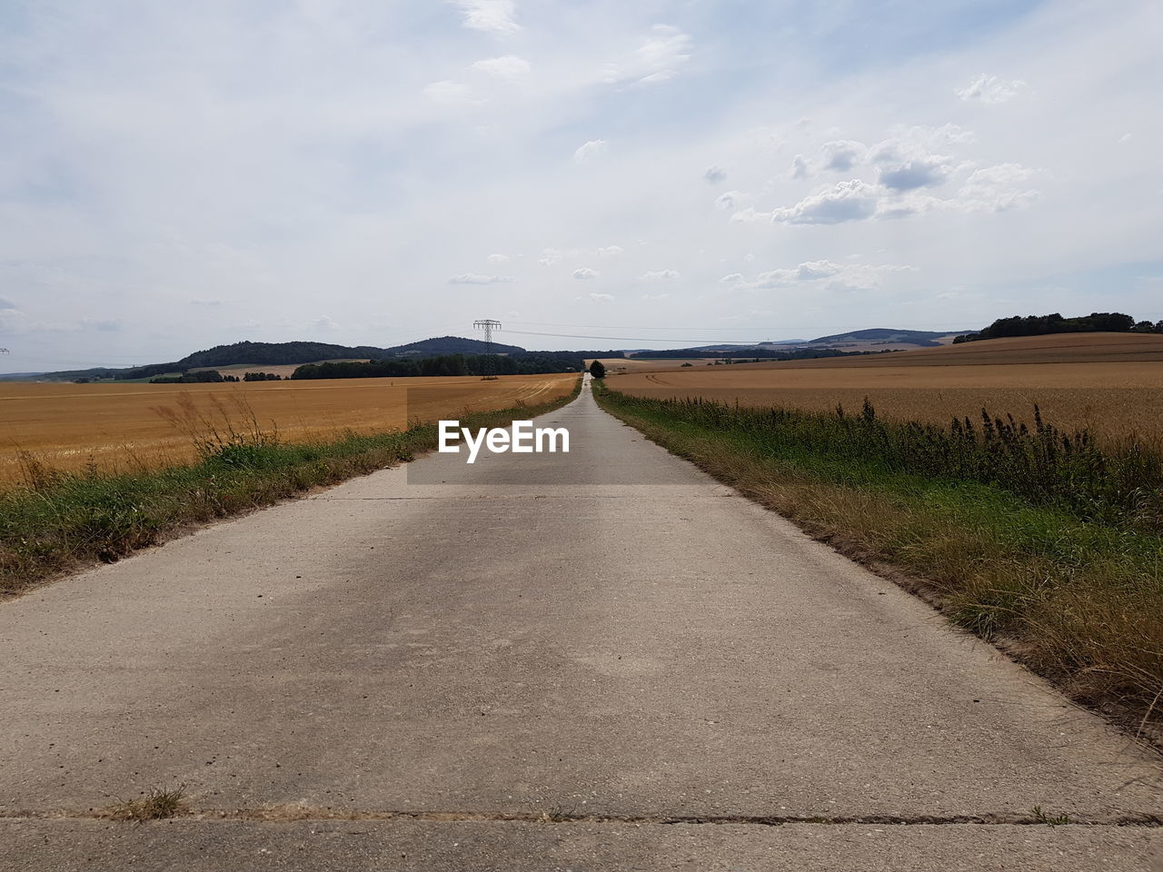 Empty road amidst field against sky