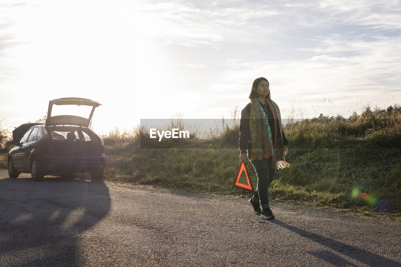 Woman on road holding warning triangle