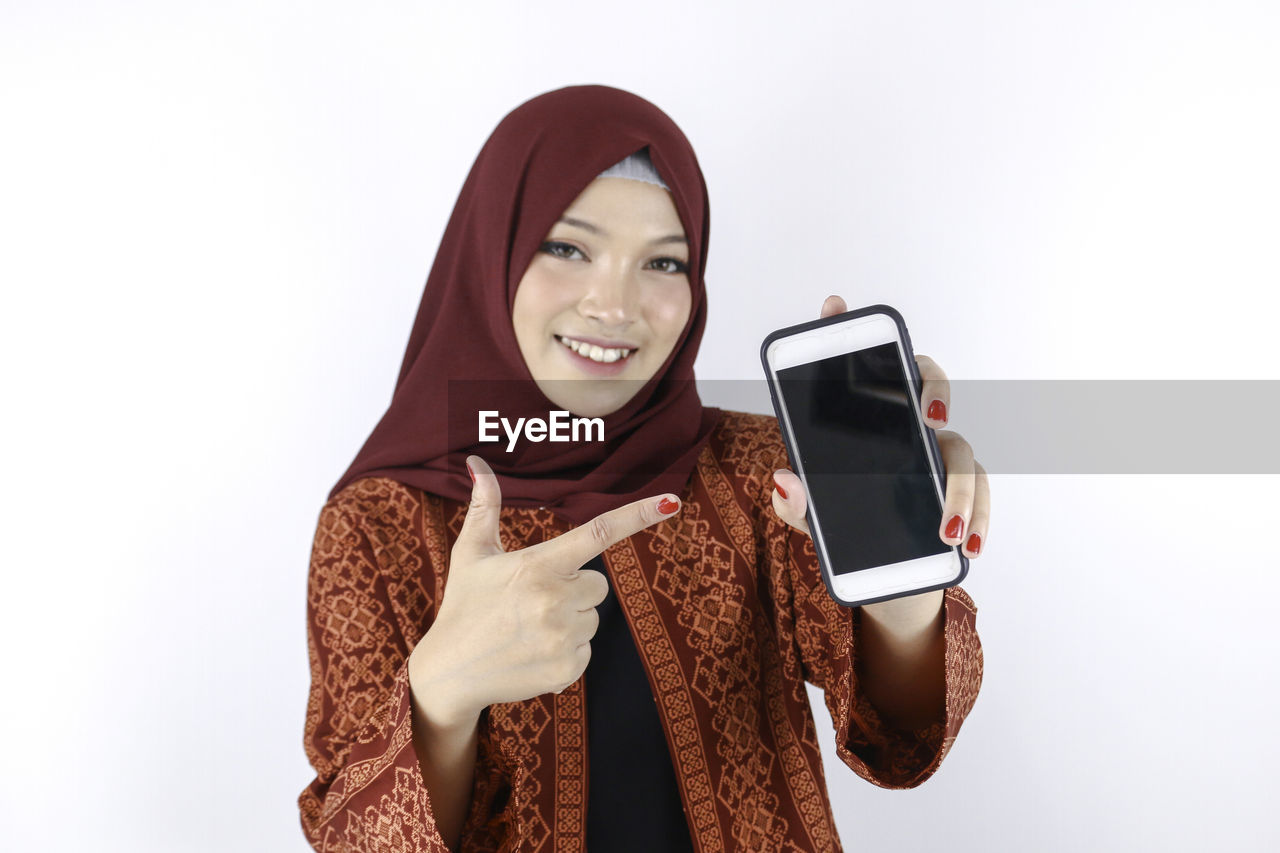 PORTRAIT OF SMILING YOUNG WOMAN USING PHONE