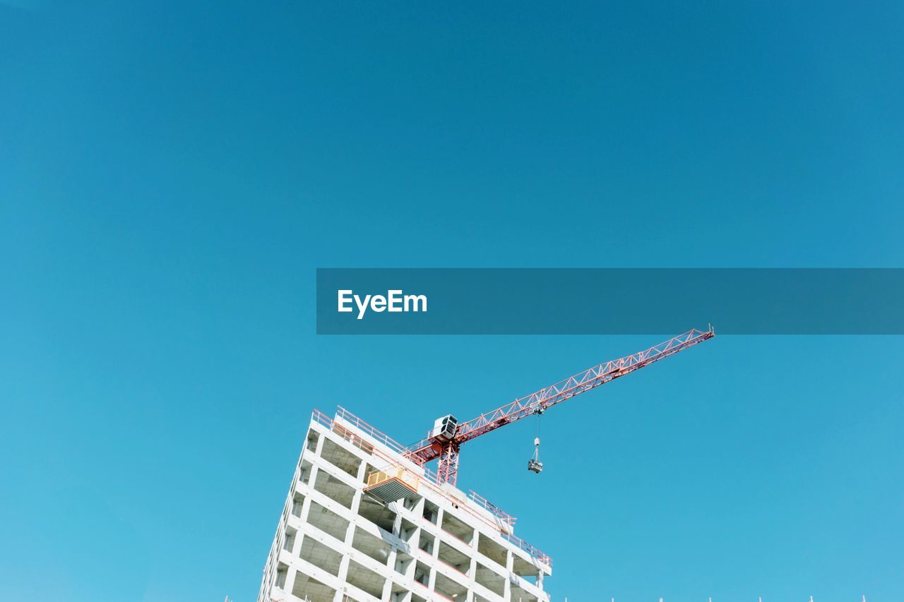 Low angle view of crane by building against clear blue sky