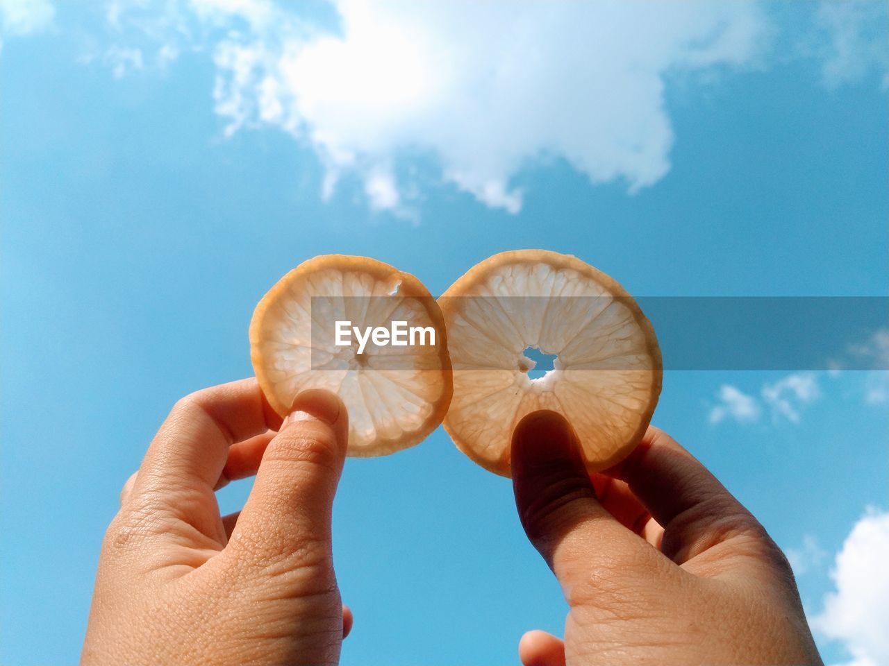 Close-up of person holding lemon slices  against sky background