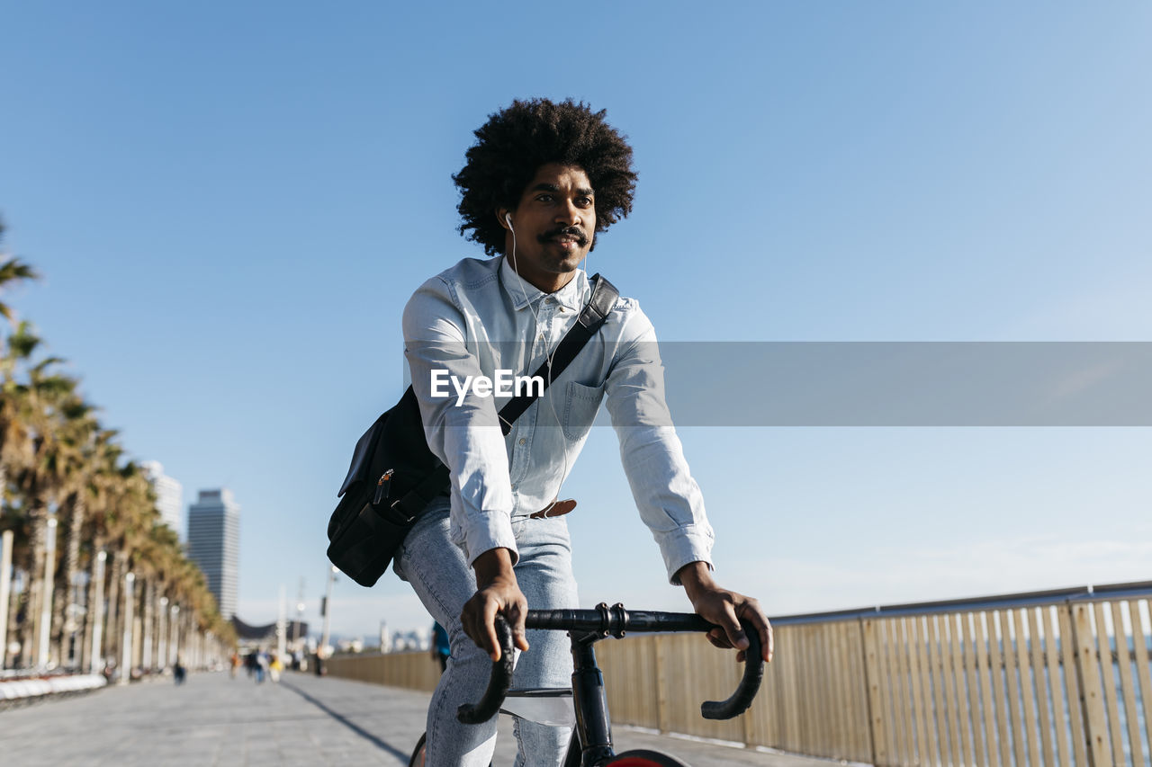 Mid adult man riding bicykle on a beach promenade, listening music