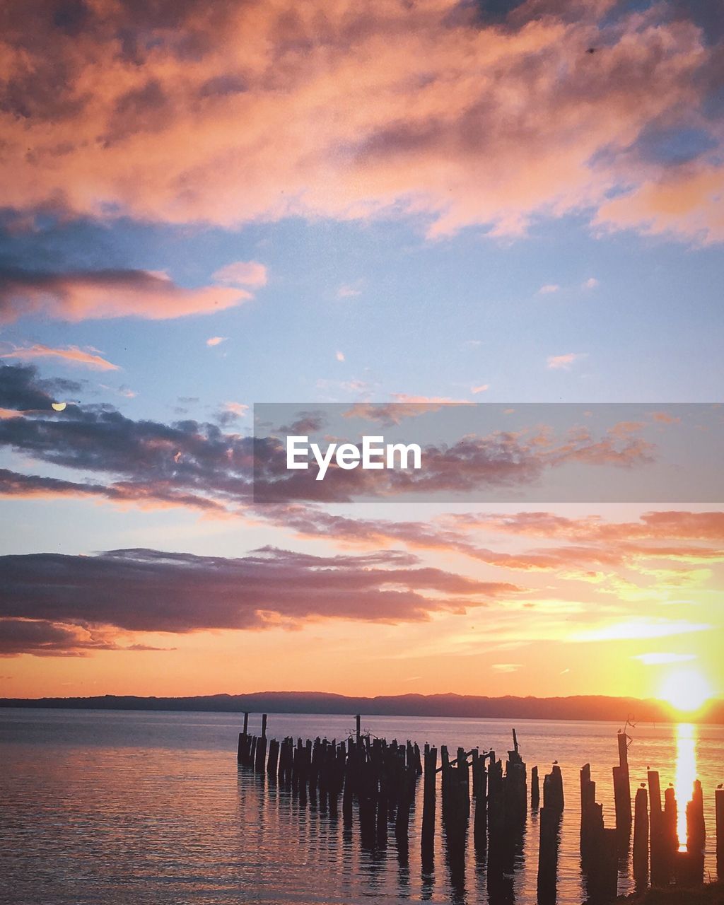 SILHOUETTE WOODEN POSTS ON SEA AGAINST SKY DURING SUNSET