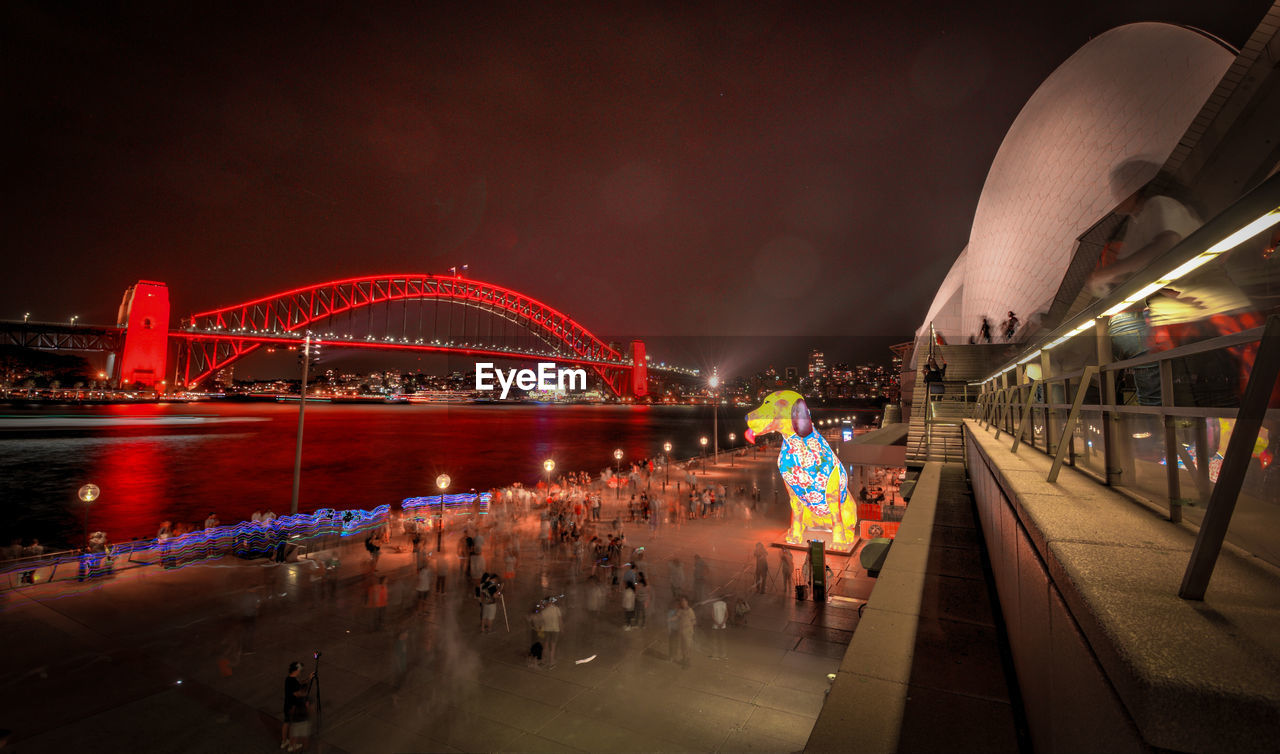 PEOPLE BY ILLUMINATED BRIDGE AGAINST SKY AT NIGHT