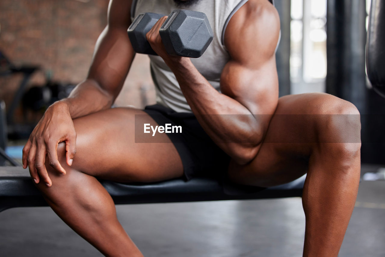 low section of woman exercising with dumbbells at gym