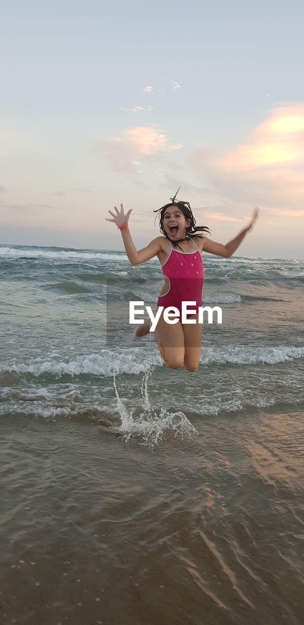 Girl jumping over sea during sunset