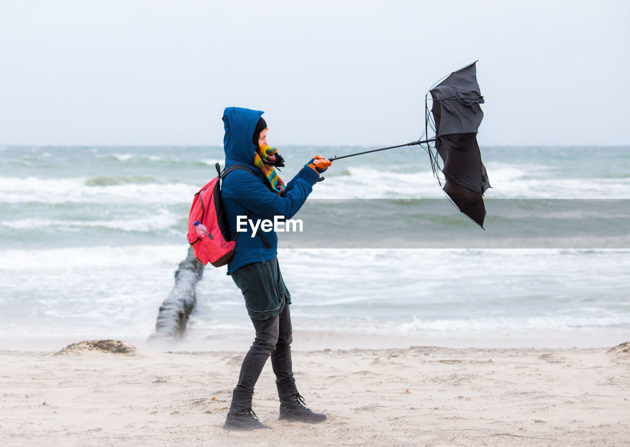 Full length of woman holding umbrella at beach during rainy season