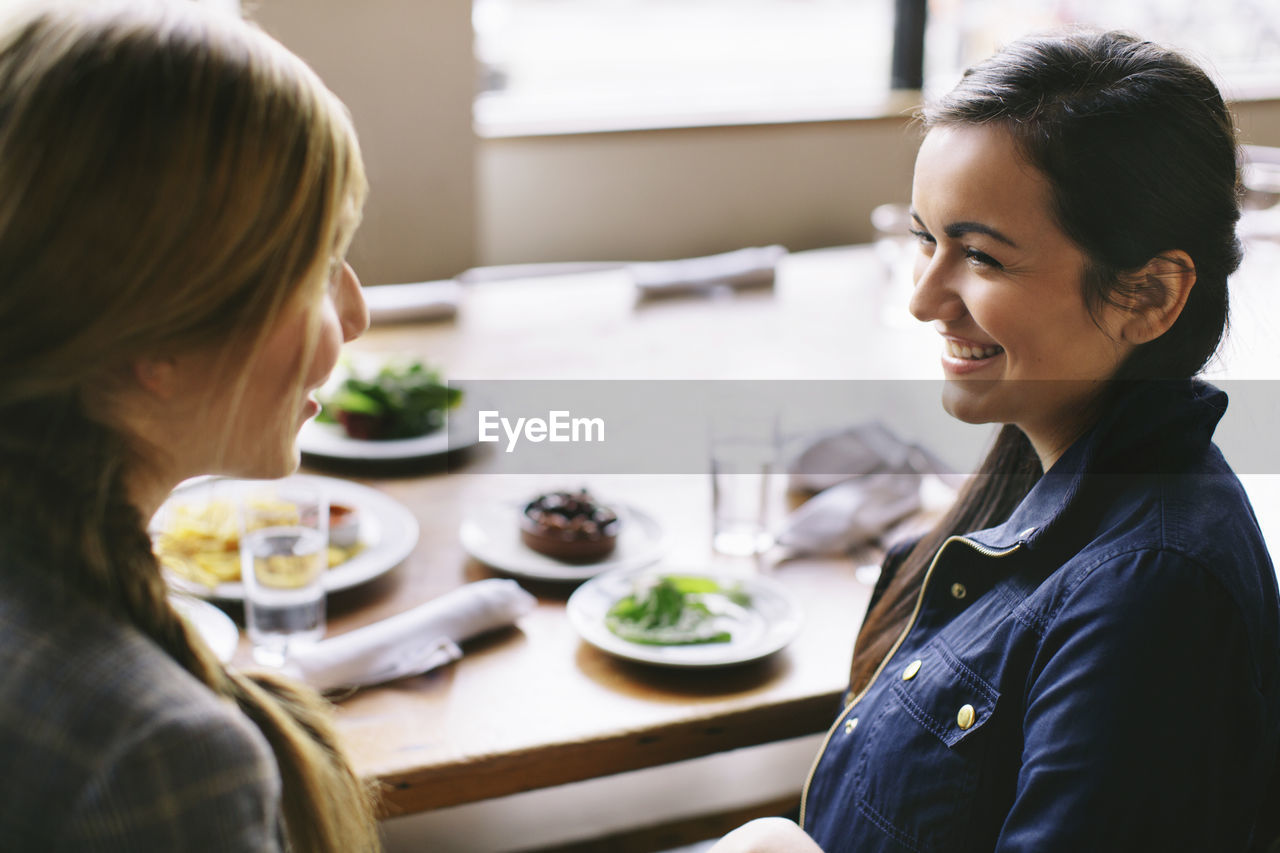 High angle view of happy female friends talking while sitting at table in restaurant