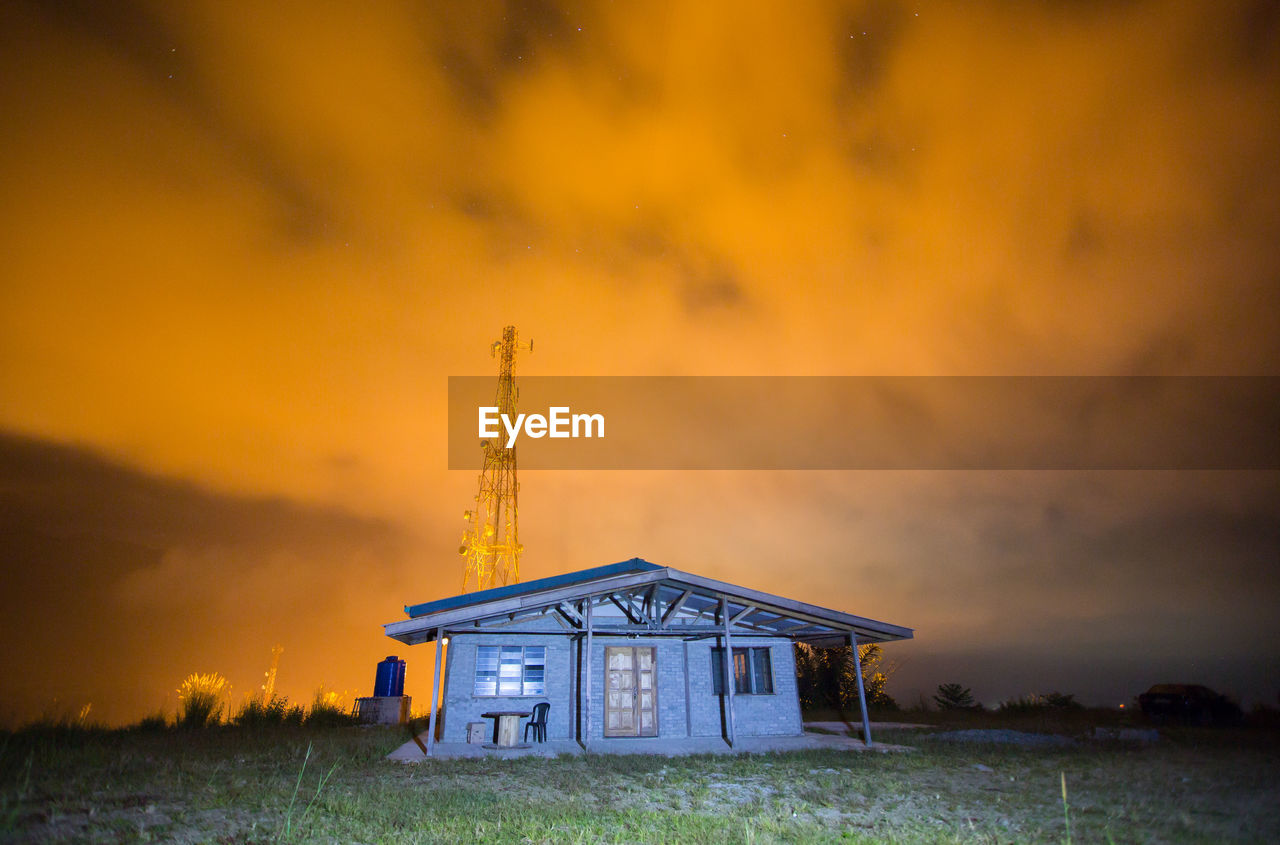 ABANDONED TOWER ON FIELD AGAINST ORANGE SKY