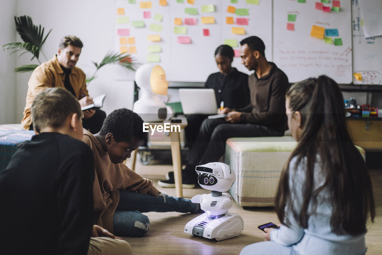 Multiracial boys and girl looking at futuristic robot on floor in innovation lab