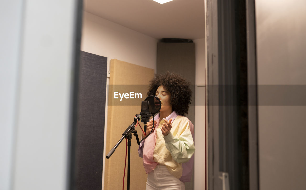 Black female singer performing song against microphone with pop filter while standing and closed eyes in sound studio