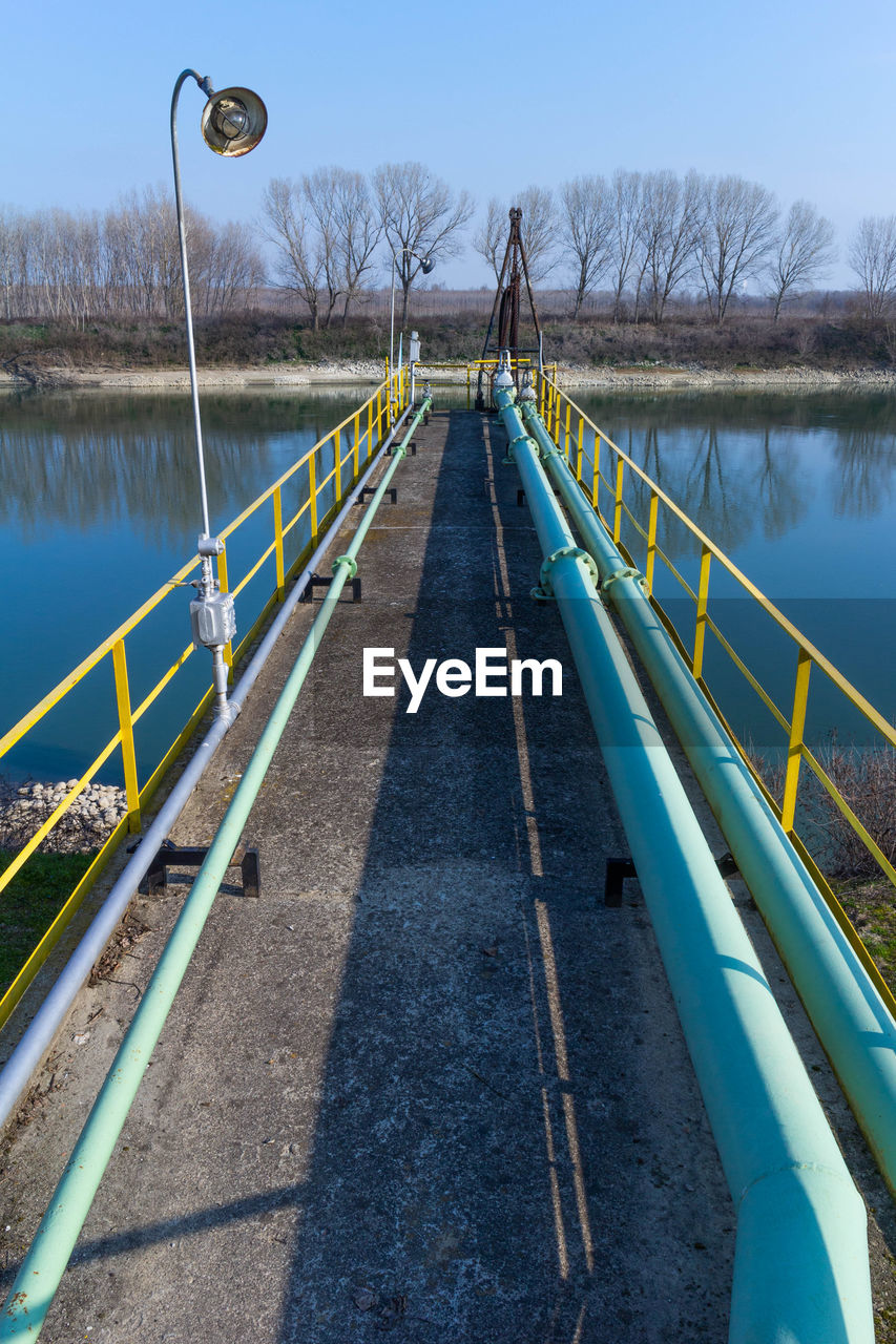 water, bridge, nature, sky, walkway, tree, waterway, day, the way forward, no people, railing, lake, transportation, outdoors, diminishing perspective, plant, architecture, blue, tranquility, reservoir, built structure, bare tree, footpath
