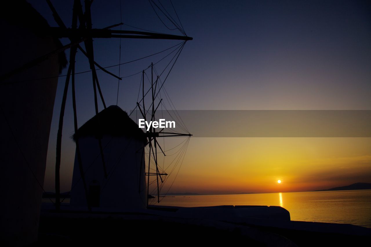 Silhouette windmills against sea at sunset