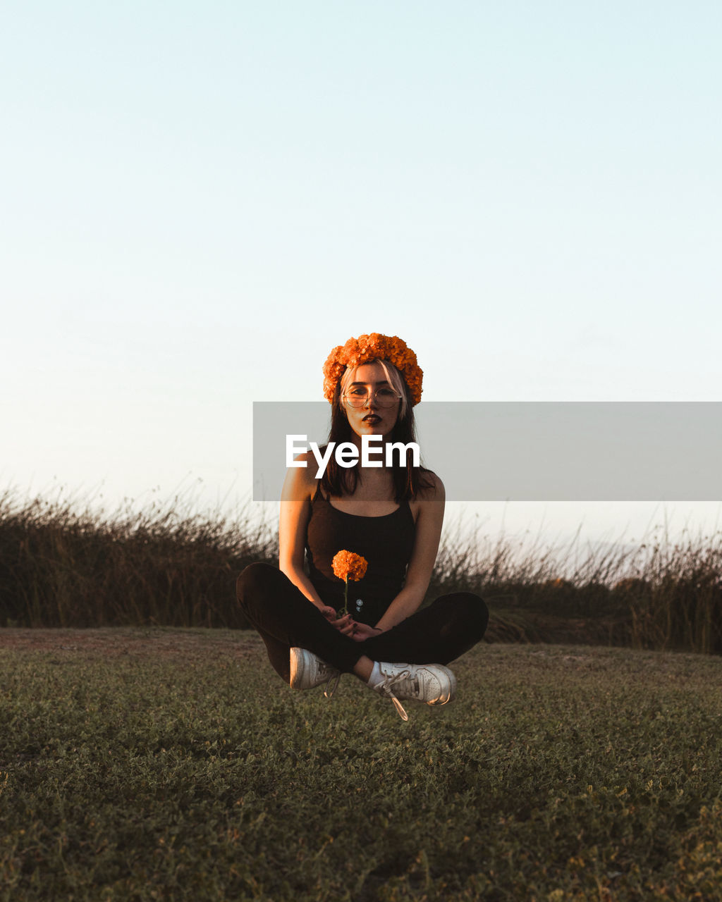 Young woman sitting on field against clear sky