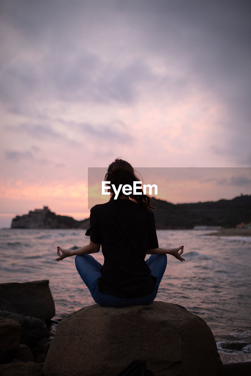 Rear view of woman doing yoga on rock at beach during sunrise