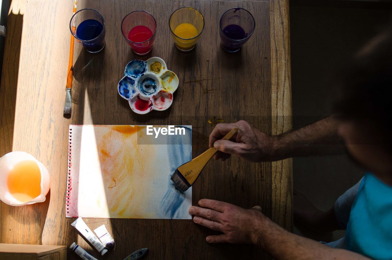 High angle view of man painting paper at wooden table