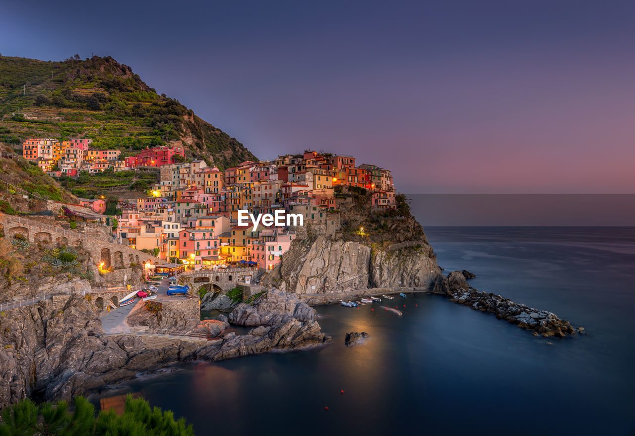 Illuminated manarola town by sea against sky during sunset