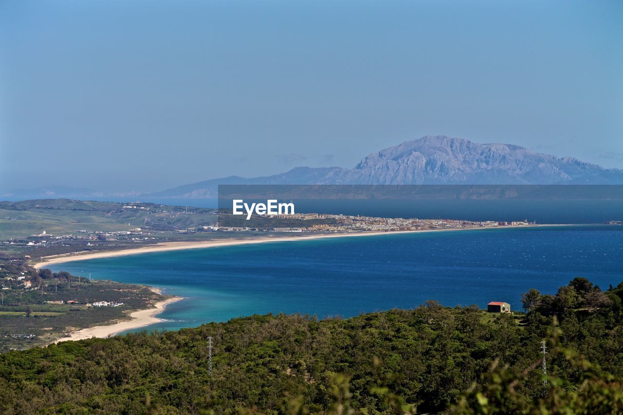 Scenic view of landscape by blue sea against clear sky