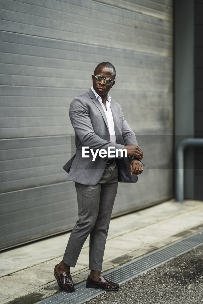 Masculine african american male executive in formal suit and sunglasses revising time on street