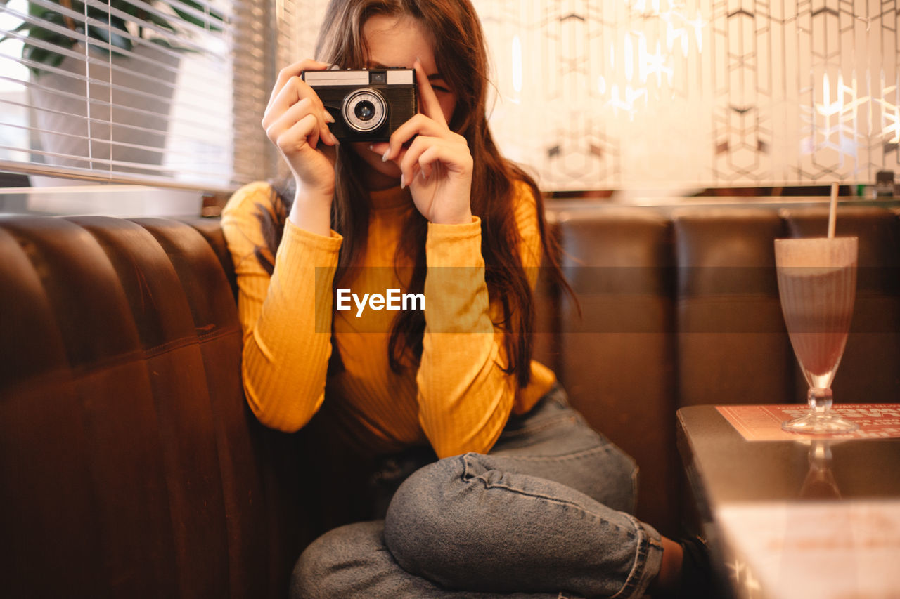 Teenage girl photographing with vintage camera while sitting in cafe