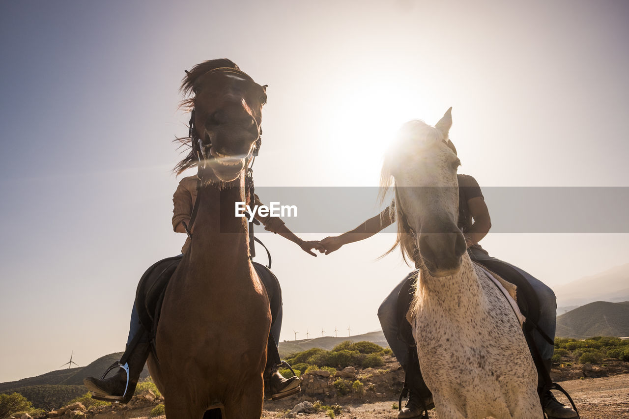 Couple riding horses on field against sky
