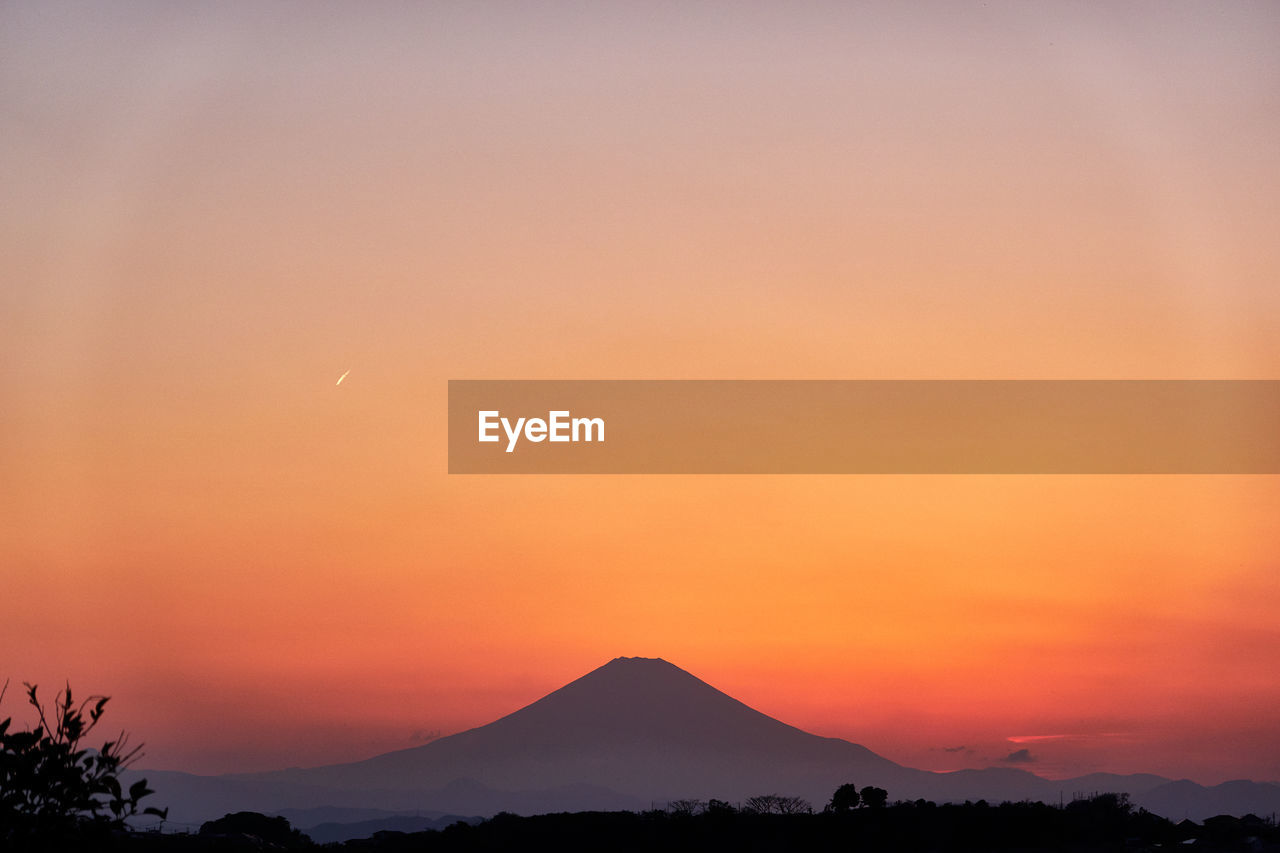 Scenic view of silhouette volcanic mountains against orange sky