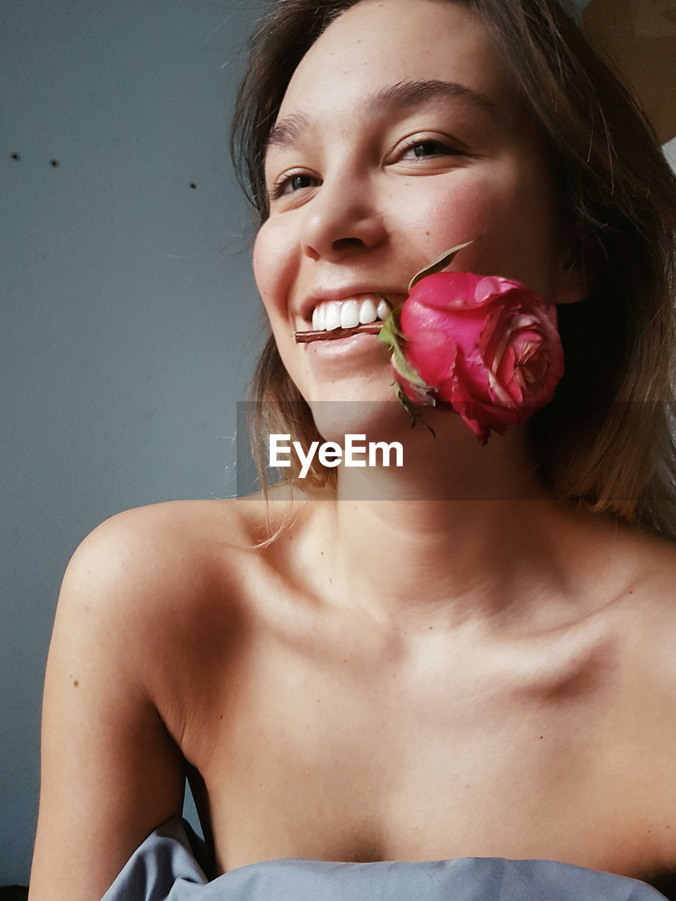 Smiling young woman carrying rose in mouth