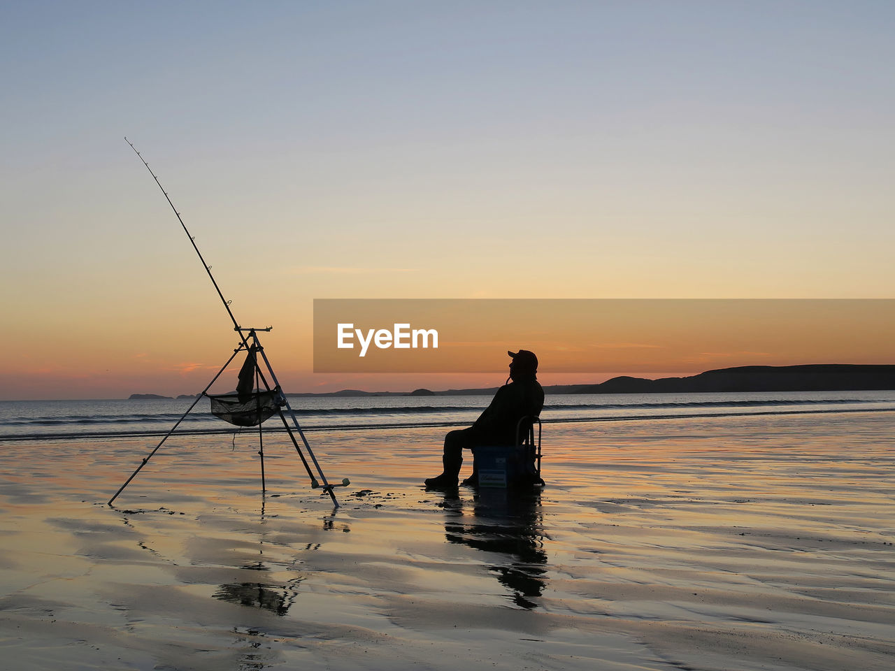 Silhouette men fishing on shore at beach against sky during sunset