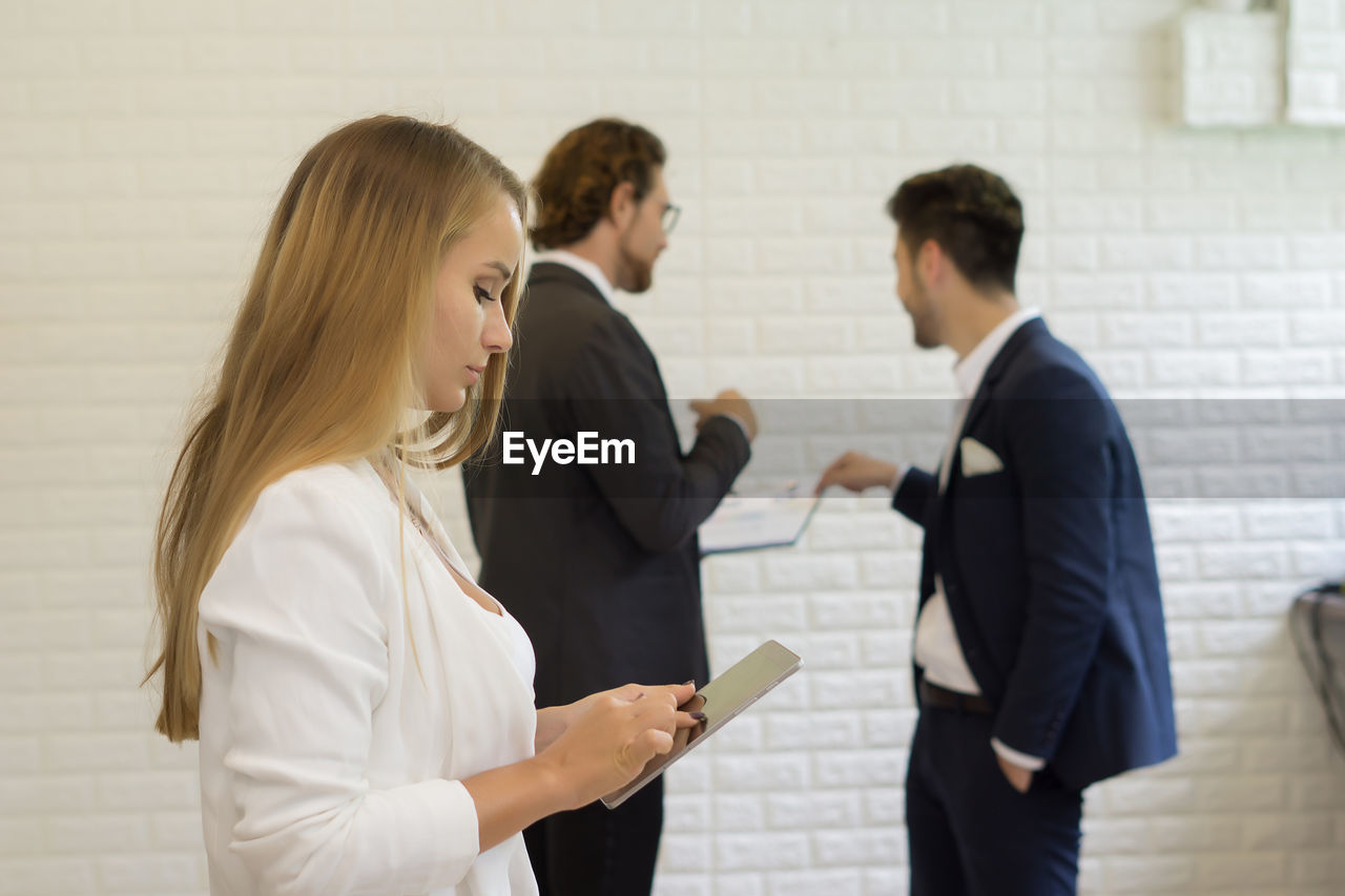 Businesswoman using digital tablet while standing with colleagues in office