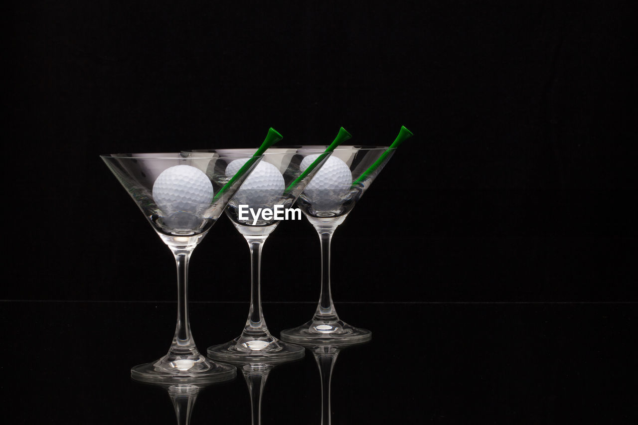 Golf balls and tees in martini glasses on black background
