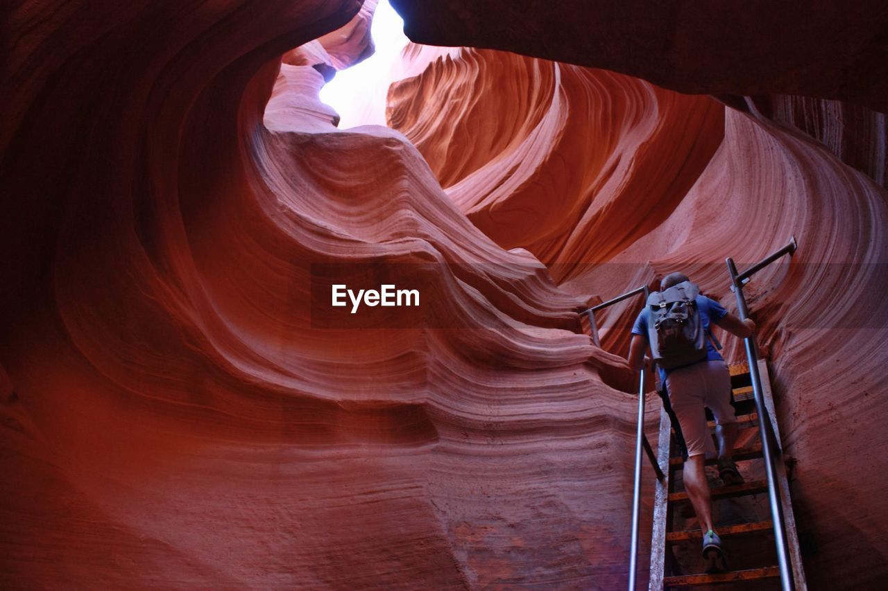 Full length rear view of tourist climbing ladder by rock formations at antelope canyon